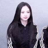 a girl with long black hair is wearing a black adidas jacket