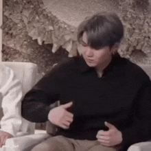 a man in a black sweater is sitting on a couch and holding his stomach .