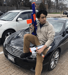 a man is sitting on the hood of a car with a nerf gun