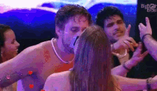 a group of people are standing around a man without a shirt while a woman kisses him .