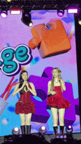 two women stand on a stage in front of a large screen that says ' ge '
