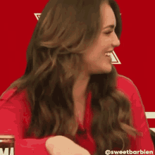 a woman in a red shirt is smiling while holding a can of beer .