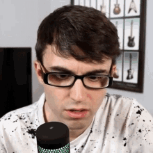 a man wearing glasses and a white shirt stands in front of a black microphone