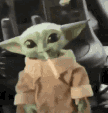 a baby yoda doll is standing in a car in front of a car .