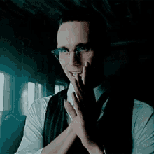 a man wearing glasses , a vest , and a tie is standing in a dark room .