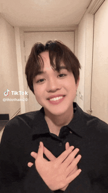 a young man in a black shirt is making a tiktok with his hands on his heart