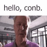 a man in a purple shirt is standing in a room with the words `` hello , conb '' written above him .