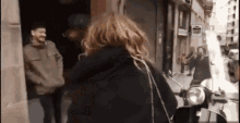 a woman is walking down a street next to a scooter and a man .