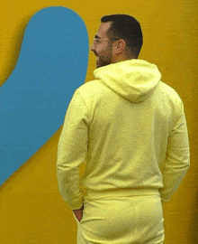 a man in a yellow hoodie is standing in front of a yellow wall