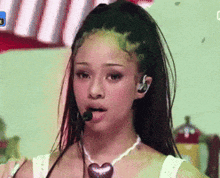 a woman wearing a heart shaped necklace and ear buds is singing into a microphone