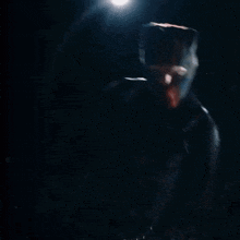 a man in a hooded jacket is holding a stack of money in his hands in the dark .