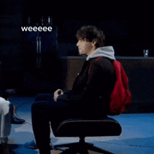 a man with a red backpack is sitting in a chair with a woman sitting next to him and the words weeeee are above him