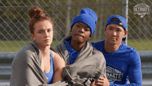 three people are wrapped in blankets and one of them is wearing a shirt that says ultimate
