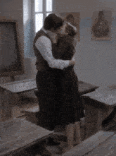 a man and a woman are kissing in a classroom with a blackboard in the background