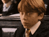 a young boy with red hair and a tie is sitting in a classroom with his eyes closed .