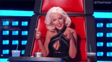 a woman in a black dress is giving a thumbs up while sitting in a red chair .