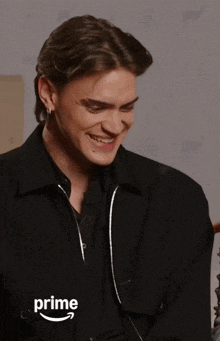 a man in a black jacket is smiling in front of an amazon prime advertisement