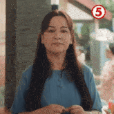 a woman in a blue shirt is standing in front of a building with a number 5 .