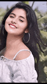 a young woman wearing hoop earrings and a white off the shoulder top smiles for the camera