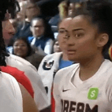 a female basketball player wearing a white jersey with the word dream on it is standing in front of a crowd .