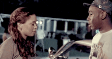 a man and a woman are looking at each other while standing next to a car .
