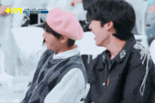 two young men are sitting next to each other in a stadium . one of the men is wearing a pink beret .