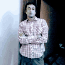 a man in a plaid shirt is standing with his arms crossed in front of a wall .