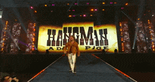 a man walks down a runway in front of a large screen that says hangman pige