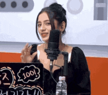 a woman is talking into a microphone in front of a laptop that says 100 on it