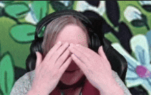 a woman wearing headphones covering her eyes with her hands