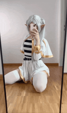 a woman taking a selfie in front of a mirror wearing a white elf costume