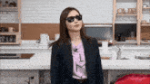 a woman wearing sunglasses is standing in front of a kitchen with a sign that says cafe