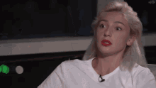 a woman with blonde hair and red lipstick is wearing a white t-shirt and sitting in a chair .
