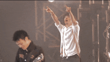 a man in a white shirt is pointing up while another man holds a guitar