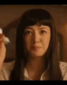 a close up of a woman 's face with long black hair and bangs .
