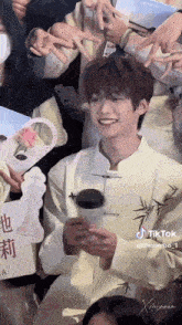 a man in a white shirt is holding a cup of coffee and smiling while standing in front of a crowd of people .