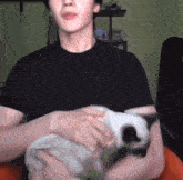 a man in a black shirt is holding a cat in his lap .
