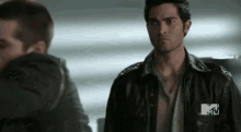 a man in a leather jacket is standing next to a man in a hoodie .
