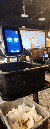 a robot with a smiley face on the screen is cleaning dirty plates in a restaurant
