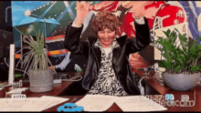 a woman is sitting at a desk with her arms in the air and a blue car in front of her