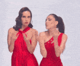 two women in red dresses are standing next to each other and blowing a kiss .