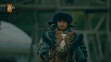 a man in a fur hat is riding a horse with a tv logo in the background