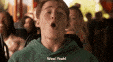 a boy in a green hoodie says woo yeah in front of a crowd