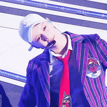 a man wearing a purple striped jacket and a red tie has a microphone in his mouth