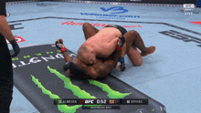 two men are wrestling on a mat with a monster logo on it