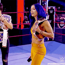 a woman with blue hair is standing in a wrestling ring holding a wrestling belt .