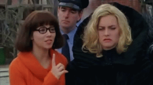 a couple of women are standing next to each other in front of a police officer . one of the women is wearing glasses .