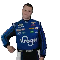 a man wearing a blue kroger racing suit stands with his hands on his hips