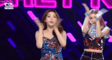 two young women are dancing on a stage in front of a neon sign .