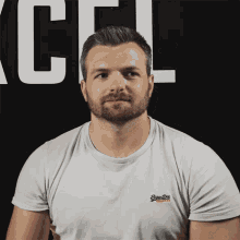 a man wearing a white superdry t-shirt stands in front of a black wall